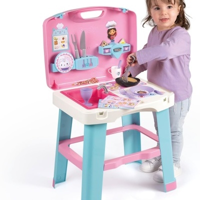 Cozinha de brinquedo infantil com utensílios coloridos e criança a brincar.