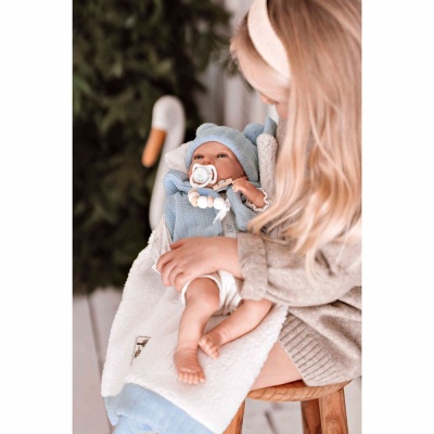 Bebé em roupa de malha azul com capuz com orelhas, manta branca e mulher loira a segurar o bebé sentada num banco de madeira