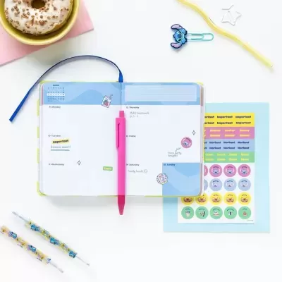 Agenda semanal aberta com caneta e autocolantes, donut, colher amarela num fundo branco