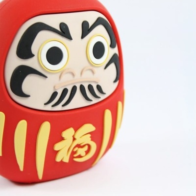 Figura Daruma vermelha com detalhes amarelos e pretos sobre fundo branco