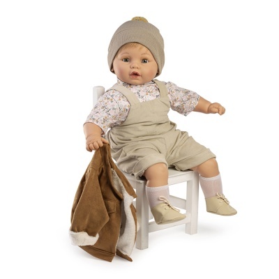 Boneco bebé sentado numa cadeira branca com roupas bege, floral e castanho segurando casaco castanho.
