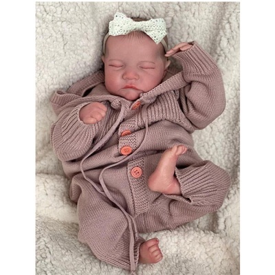 Bebé com fato de malha rosa e fita branca na cabeça sobre manta branca felpuda