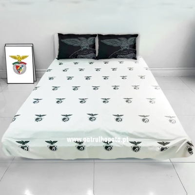 Cama com lençol branco e almofadas pretas com estampas do logótipo do SL Benfica