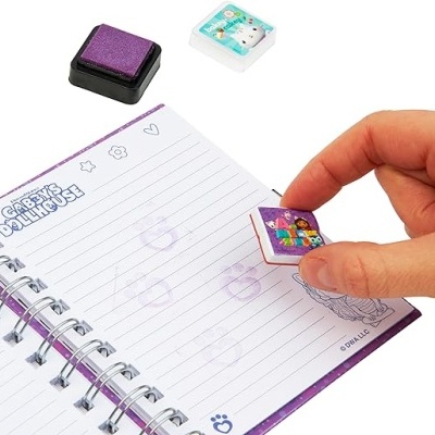 Mão carimbando caderno com carimbo colorido, carimbos roxo e branco ao fundo