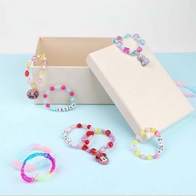 Pulseiras coloridas de contas com palavras e elásticos exibidas junto a caixa bege.