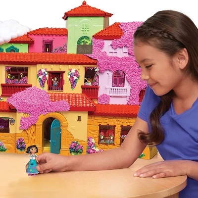Casa de brinquedo colorida com boneca a brincar, sobre mesa com criança ao lado