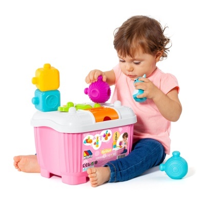 Criança a brincar com brinquedo de encaixe colorido em caixa rosa com tampa branca.