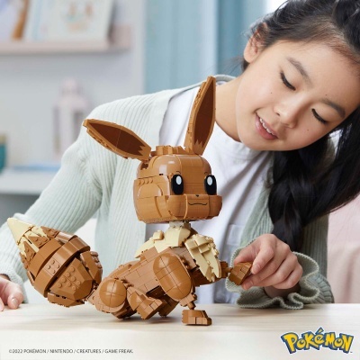 Figura de construção de Eevee Pokémon em blocos castanhos e creme sobre mesa com menina a brincar