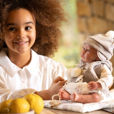 Menina segurando boneca realista vestida de cinzento e branco numa mesa com limões