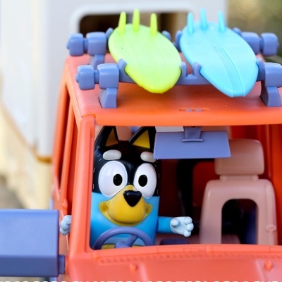 Personagem animado a conduzir carro de brinquedo laranja com pranchas de surf no tecto