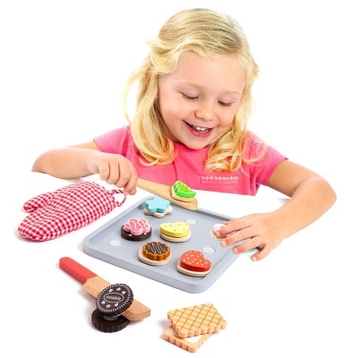 Criança a brincar com bolos e biscoitos de madeira coloridos sobre tábua cinzenta