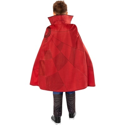 Criança de costas usando um manto vermelho com padrão geométrico, calças pretas e sapatos pretos.