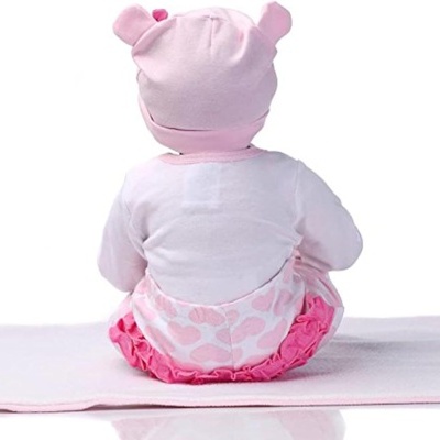 Boneca bebé vestida de rosa sentada de costas sobre manta rosa