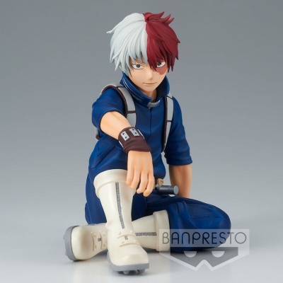Figura colecionável de personagem masculino com cabelo bicolor e roupa azul em posição de sentado.