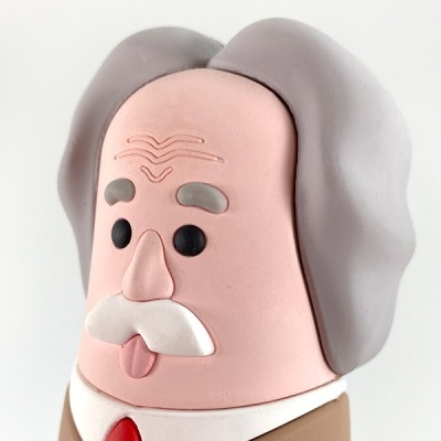 Figura de homem com bigode e cabelo cinzento, gravata vermelha e bolso com canetas.