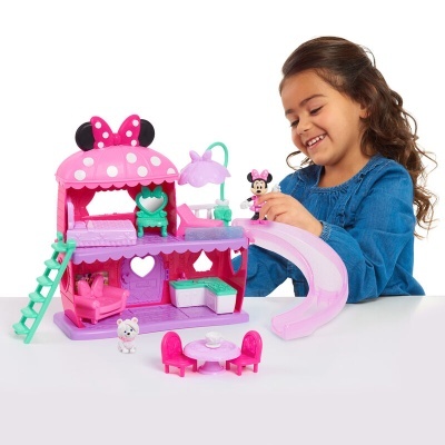 Brinquedo casa de bonecas cor-de-rosa e lilás com figuras e acessórios, criança a brincar.