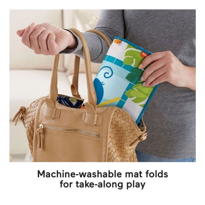 Manta dobrável colorida com padrão de animais e folhas sendo colocada numa mala de mão bege trançada