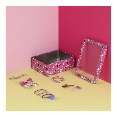 Caixa de metal rosa com padrão e acessórios de cabelo coloridos sobre superfície amarela