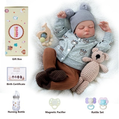 Boneco bebé realista com roupa cinzenta e castanha e vários acessórios para bebé.