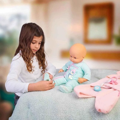 Menina com boneca de bebé vestida de azul claro sobre manta cinzenta com roupa rosa ao lado