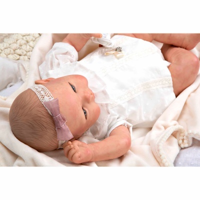 Boneca bebé com vestido branco e faixa de cabelo rosa deitada em tecido branco