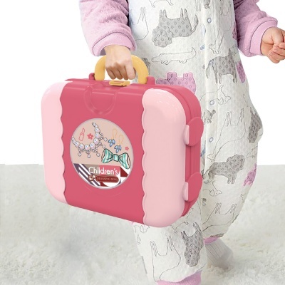 Mala de brinquedo rosa com alça amarela segurada por criança em pijama branco com padrões de animais