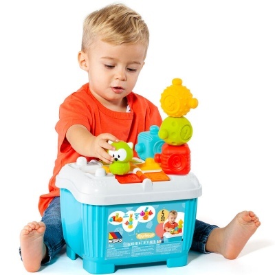 Menino brincando com caixa de brinquedo azul e peças coloridas em branco