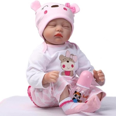 Boneca bebé vestida com pijama e gorro rosa, ao lado de biberão com tampa rosa