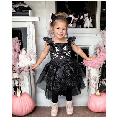 Menina com vestido preto de gato e arco com orelhas entre abóboras e flores cor-de-rosa