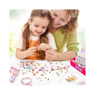 Contas de bijuterias coloridas e fios numa mesa com criança e adulto