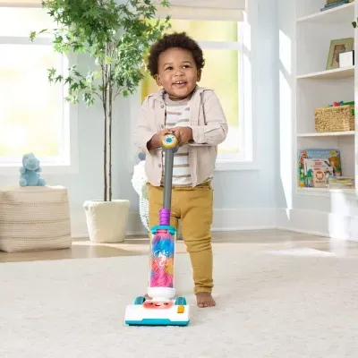 Criança com aspirador de brinquedo colorido em quarto com estante e planta