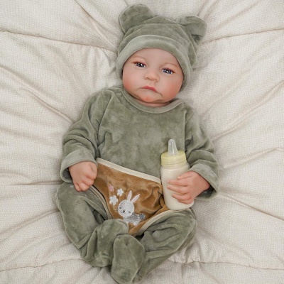 Bebé de veludo verde com capuz e biberão numa almofada creme