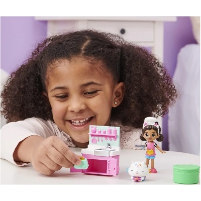 Criança a brincar com brinquedos de cozinha em miniatura e figuras coloridas numa mesa branca