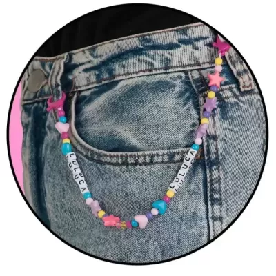 Corrente colorida com contas e letras LULUCA pendurada em jeans azul claro