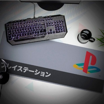 Tapete para rato PlayStation com logotipo e texto em japonês sobre mesa com teclado, caneca e auscultadores