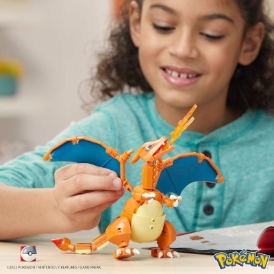 Brinquedo de construção Charizard com asas azuis e barriga amarela, nas mãos de uma criança, sobre mesa clara em ambiente interior.