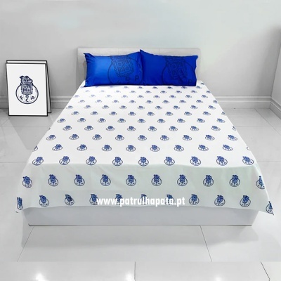 Cama com lençol branco estampado com logotipos azuis e duas almofadas azuis num quarto minimalista
