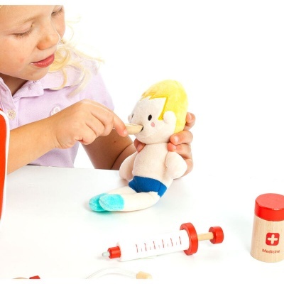 Criança a brincar com boneca de peluche e brinquedos médicos numa mesa branca