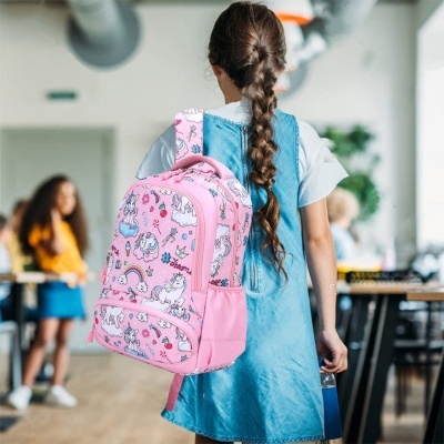 Mochila escolar rosa com unicórnios e arco-íris numa criança vestida com vestido azul