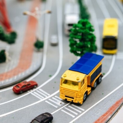 Modelo miniatura de camião amarelo em estrada de brinquedo com árvores e carros miniatura