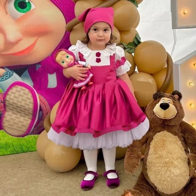Menina com vestido rosa e touca segurando boneca rosa, com urso de peluche castanho ao lado
