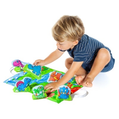 Criança a brincar com brinquedos de tecido de dinossauros coloridos num tapete verde.