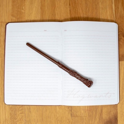 Caderno aberto com caneta castanha em forma de varinha sobre mesa de madeira