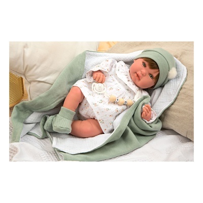 Boneca bebé realista com roupa branca e acessórios verdes sobre manta verde