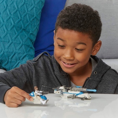 Menino brincando com brinquedo branco com detalhes azuis em mesa branca diante de sofá cinzento com almofadas azuis