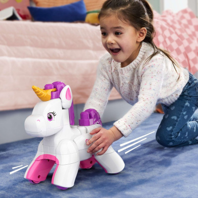 Brinquedo unicórnio de plástico branco com detalhes rosa, roxo e amarelo, com rodas, em tapete azul, criança brincando