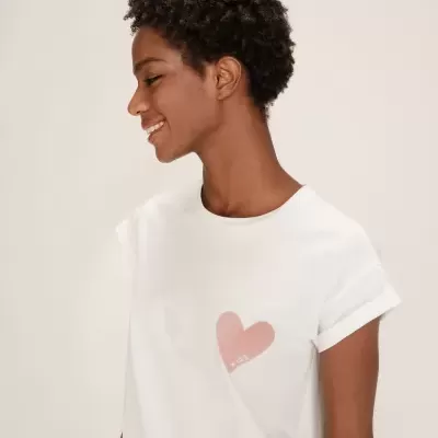 Mulher de perfil a usar t-shirt branca com coração rosa estampado e palavra KISS