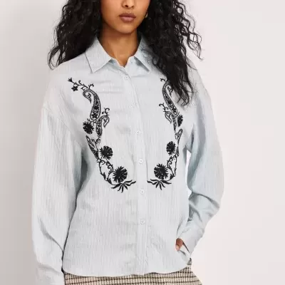 Camisa azul clara de manga comprida com bordados florais pretos e saia xadrez bege e preta