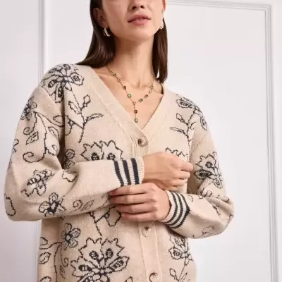 Cardigã bege com padrão floral preto e botões grandes, com mujer a usar colar e brincos