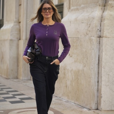 Mulher com blusa roxa e calças pretas a caminhar num cenário urbano